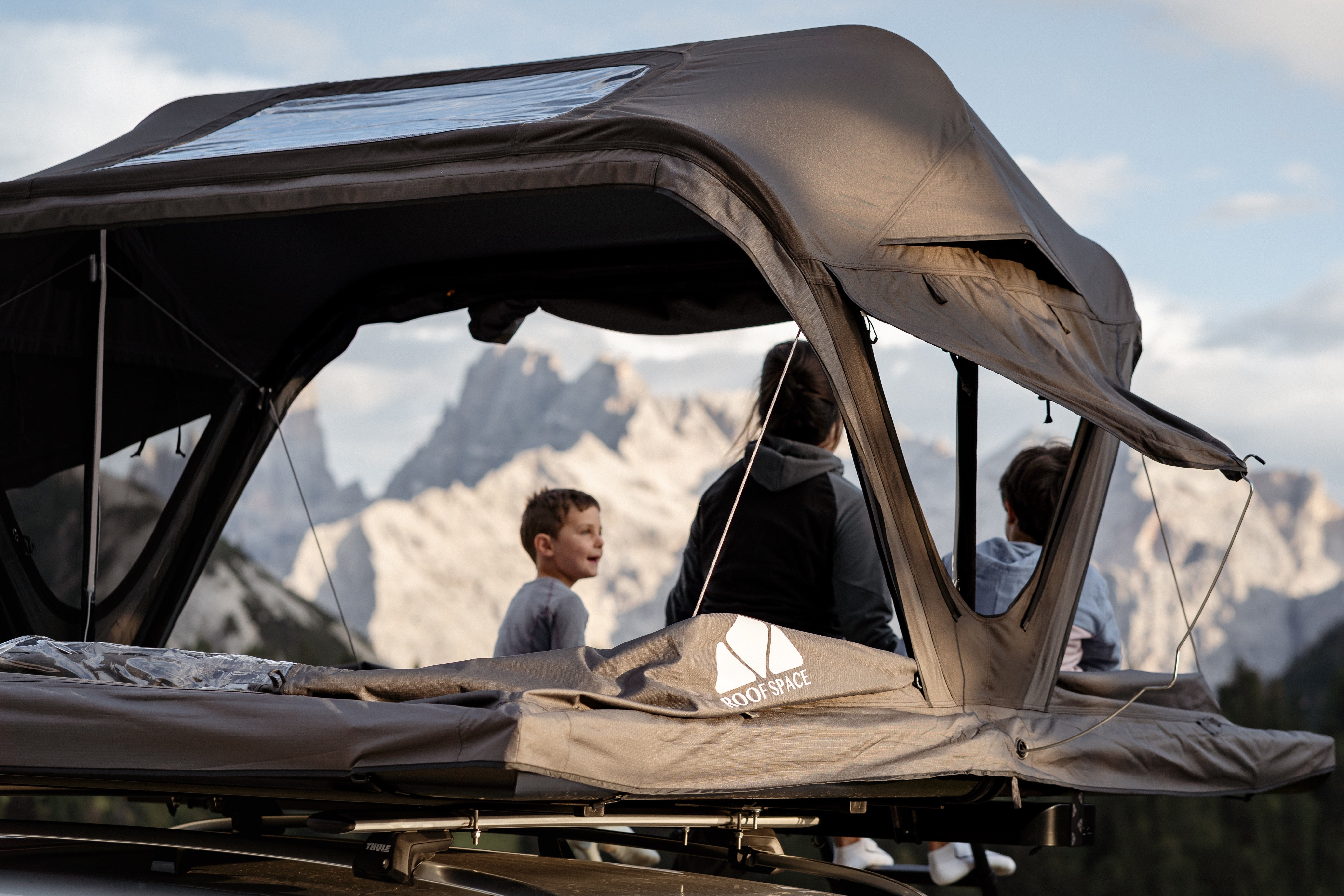Graues Auto mit Dachzelt vor alpiner Bergkulisse. Camping-Lifestyle für Abenteuer und unvergessliche Momente in der Natur.