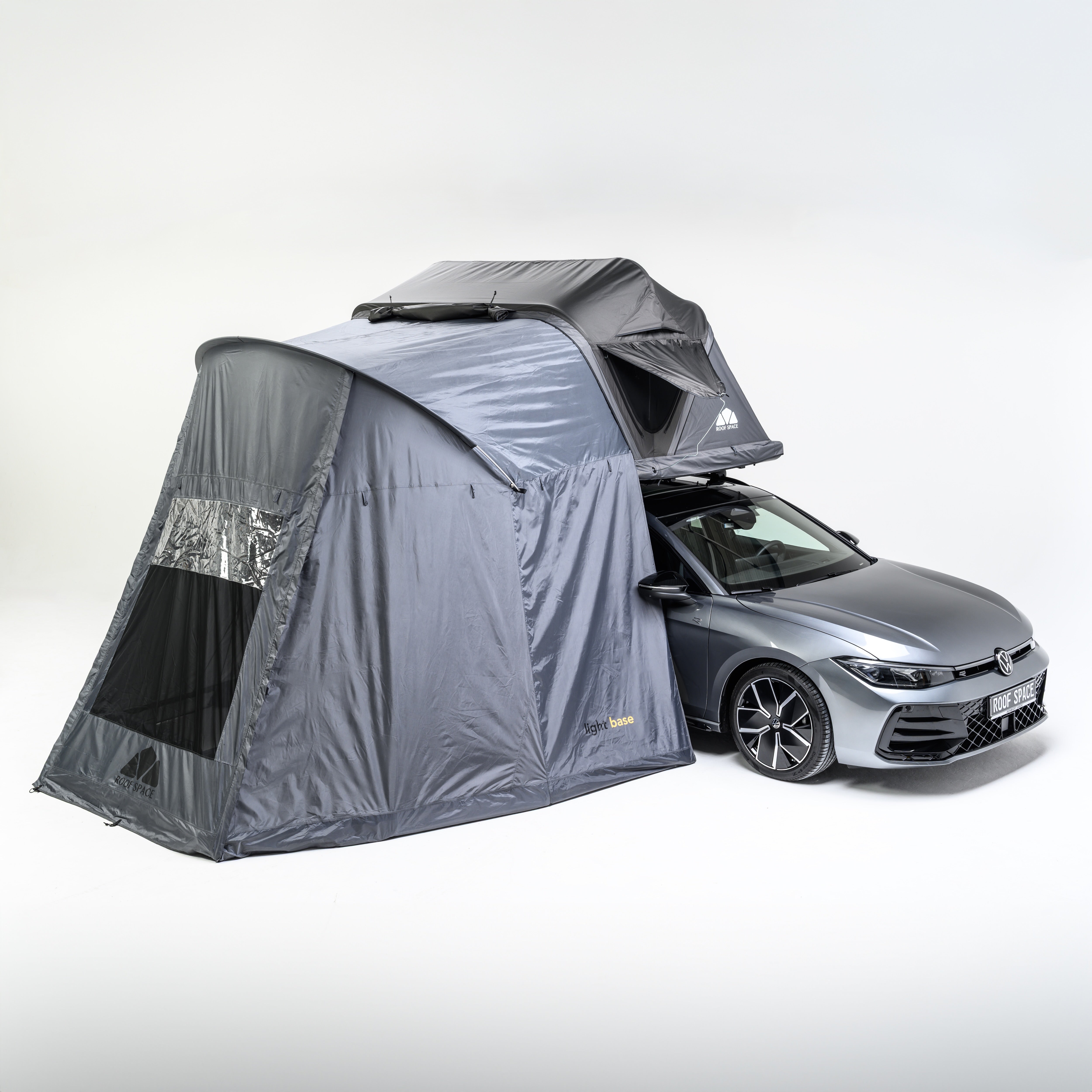 Ein graues Auto mit einem grauen Dachzelt und einem daran befestigten Vorzelt vor einem weißen Hintergrund. Text sichtbar: "light base" und "ROOF SPACE".