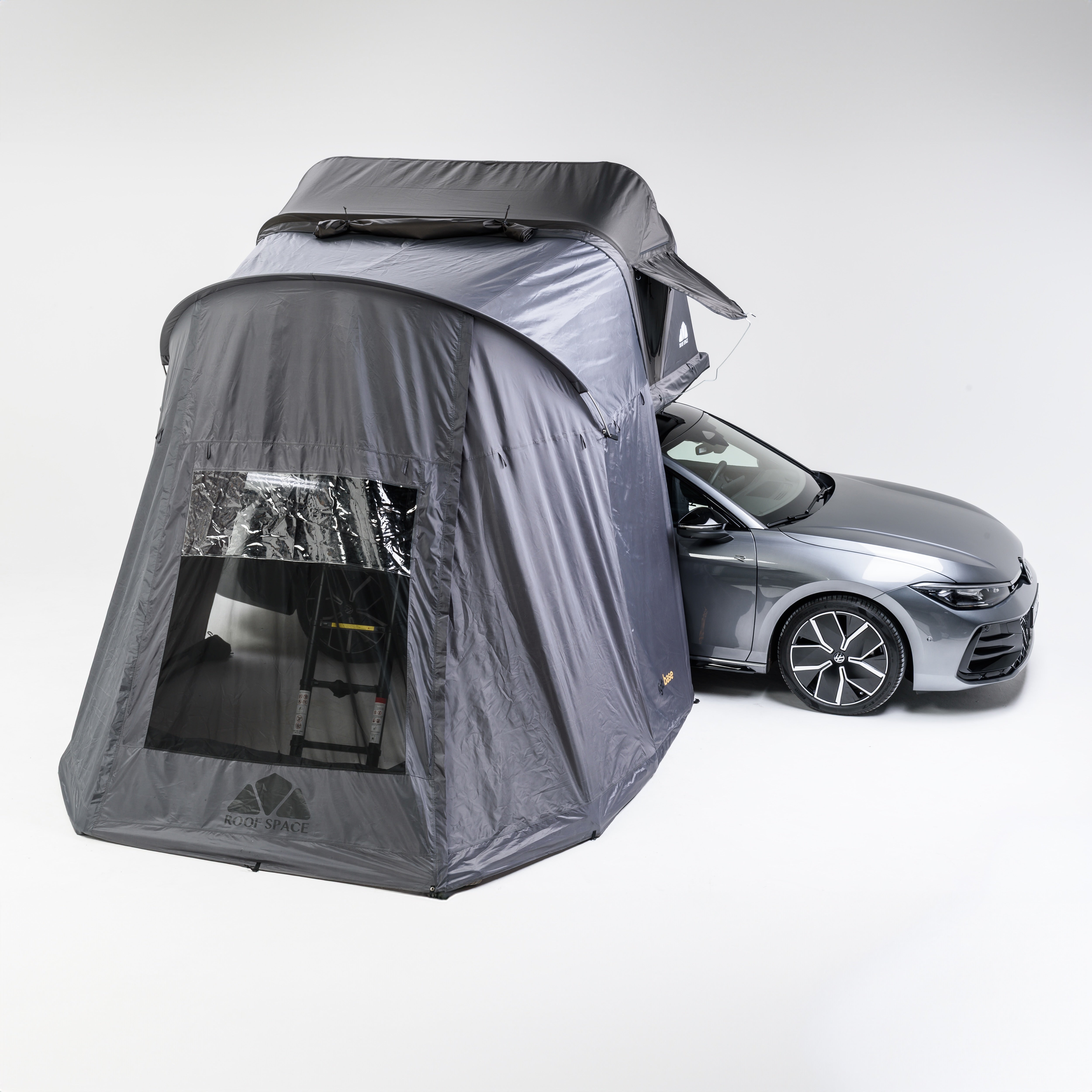 Ein graues Auto mit Dachzelt und Zeltanbau vor weißem Hintergrund. Das Zelt hat ein Fenster mit Blick auf eine Leiter. Auf dem Zelt steht "ROOF SPACE".